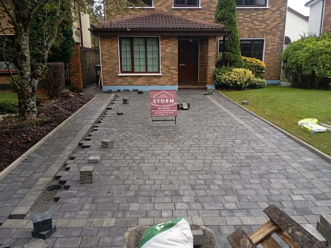 During: the same driveway mid-lay, loose blocks and a Storm site sign