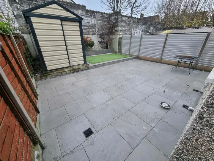 Grey paved patio with a linear drain, shed and block walls